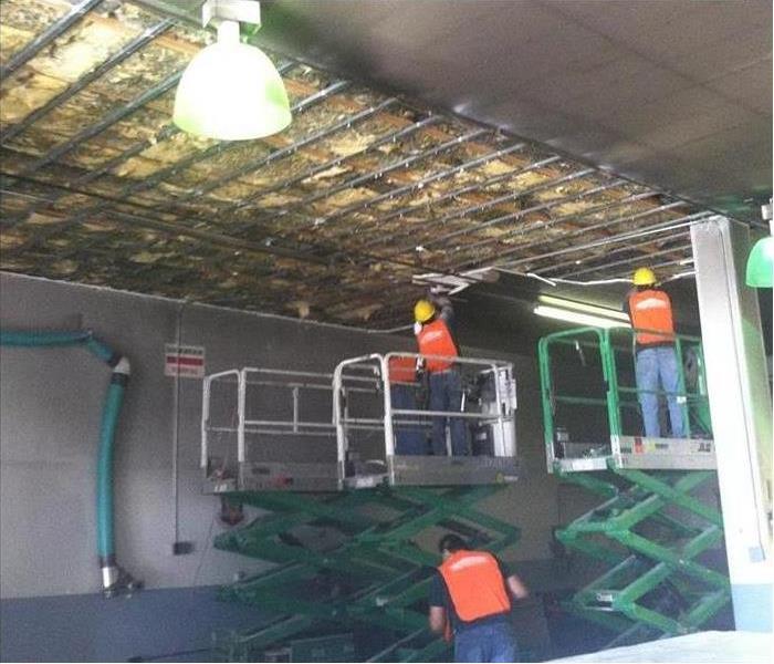 Two SERVPRO team members elevated and cleaning off fire damaged ceiling.